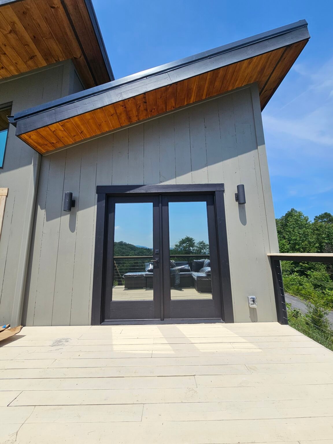 Modern home entrance with gray vertical siding, dark door trim and natural wood soffit