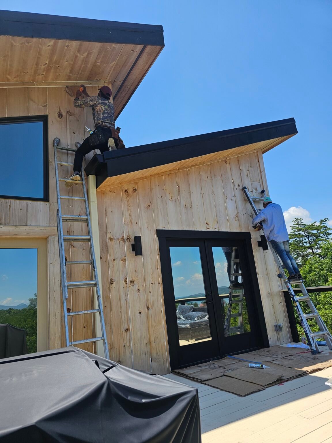 Workers preparing bare wood siding around a modern home entrance, with floor coverings in place