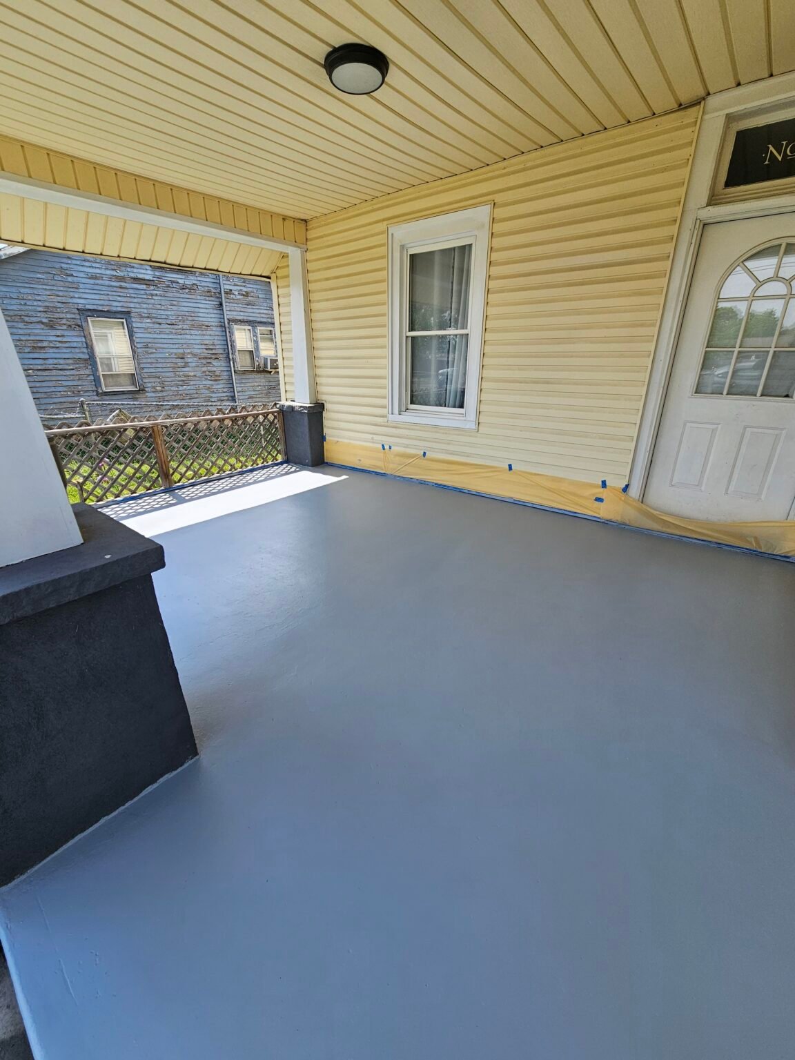 Covered porch floor with a fresh gray finish and protective masking along the siding