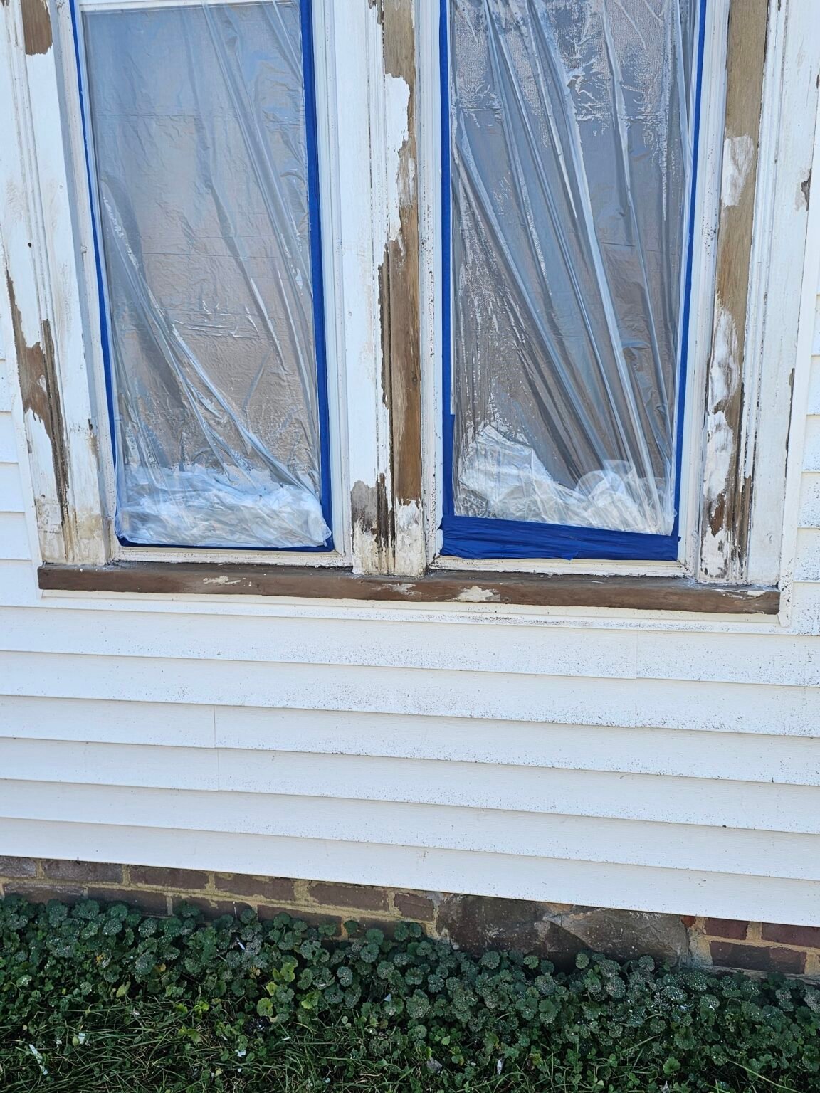 Exterior window trim during preparation, with exposed wood and plastic masking over the glass